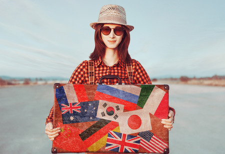 Smiling traveler woman holding suitcase. Stamps flags of different countries on a suitcase. Concept of travelの写真素材