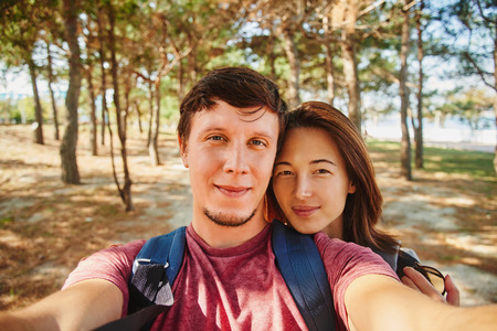 Smiling traveler young loving couple taking self-portrait in summer forestの写真素材