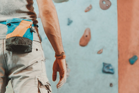 Young man standing in front of a practical climbing wall indoor and preparing to climb, close-upの写真素材