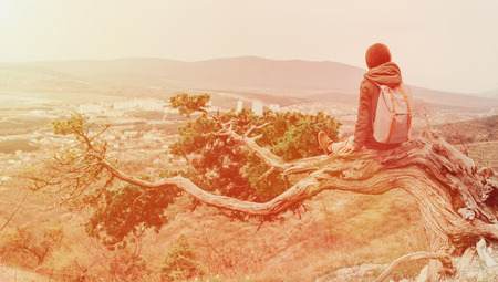 Traveler young woman sitting on a tree in the mountains. Image with sunlight effectの写真素材