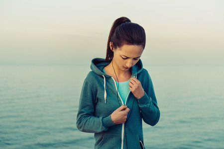 Young sportswoman in headphones workout on coastline in summer in the morning