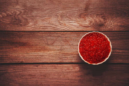 Red salmon caviar in a bowl on wooden background, top view. Space for text in left part of the imageの写真素材