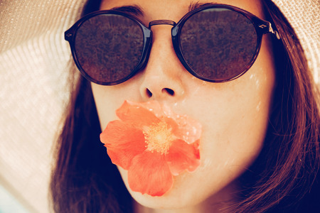 Portrait of attractive girl in sunglasses with red flower, concept of summer mood. Fashionable and beautiful summer girl. の写真素材