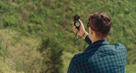 Hiker young man searching direction with a compass in summer