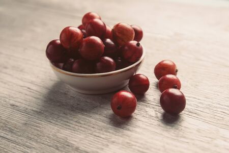 Fresh ripe red gooseberries in a bowl on wooden background
