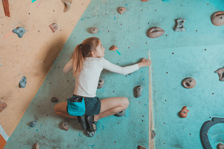 Climber little girl exercises in gym. Climber girl sitting on artificial boulders in pose of frogの写真素材