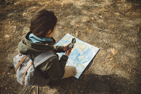 Traveler young woman with backpack searching direction with a compass on background of map in the forest. Focus on compassの写真素材