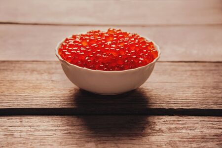 Red salmon caviar in a white bowl on wooden backgroundの写真素材