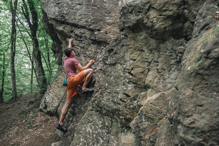 Free climber man starting to climbing on stone rock outdoor in summer, boulderingの写真素材