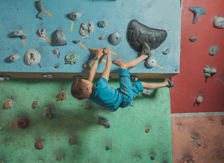 Climber boy exercises on artificial boulders wall in gymの写真素材