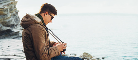 Traveler young man with photo camera sitting on coast near the seaの写真素材