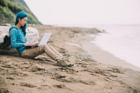 Freelancer young beautiful woman working on laptop on sand beach near the seaの写真素材