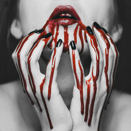 Young woman touching her face in blood. Halloween and horror theme. Black and white image with red elementsの写真素材