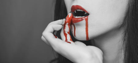 Vampire woman wipes the blood from her lips. Halloween or horror theme. Black and white image with red elementsの写真素材