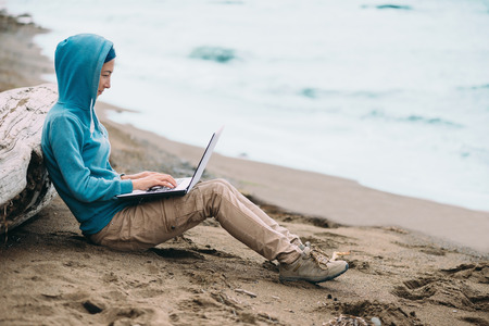 Freelancer young woman working on laptop on beach near the sea. Freelance conceptの写真素材