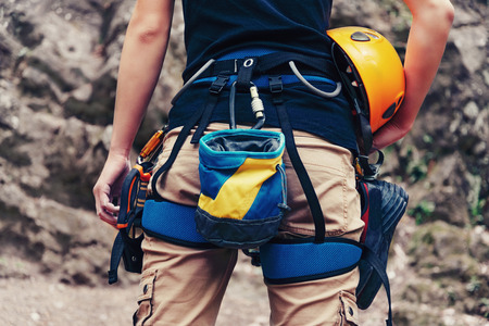 Woman standing with climbing equipment and helmet in front of stone rock outdoor, rear view. Close-up. Face is not visibleの写真素材
