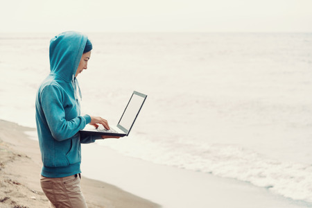 Freelancer girl standing on beach near the sea and working on laptop. Freelance conceptの写真素材