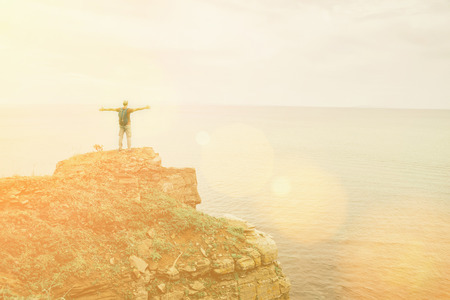 Happy traveler man standing  with raised arms on peak of rock and enjoying view of sea. Image with...