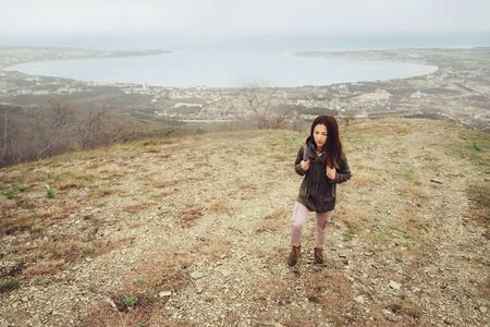 Hiker young woman with backpack walking up on mountain over the bay outdoorの写真素材