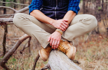 Unrecognizable traveler young man sitting on tree trunk, view of legsの写真素材