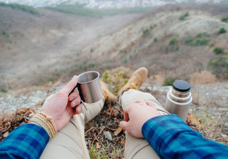 Hiker young man with cup of tea and flask resting in the mountains.の写真素材