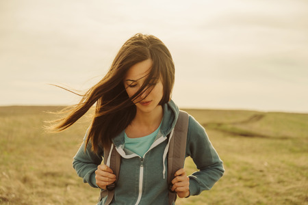 Beautiful young woman with backpack walking on meadow. Portrait of hiker girl outdoorの写真素材