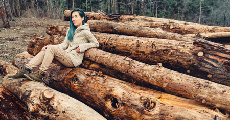 Young woman with blue hair sitting on stack of tree trunk, girl resting outdoorの写真素材