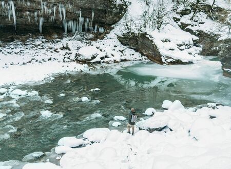 Hiker girl with backpack standing near the mountain river and enjoying view of nature in winter.の写真素材