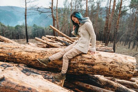 Smiling girl with blue hair sitting on fallen tree trunk. Young woman resting outdoorの写真素材
