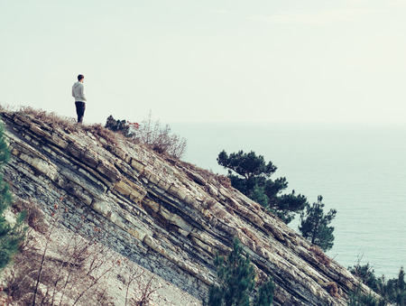 Young man standing on a rock coast outdoor and looking at seaの写真素材