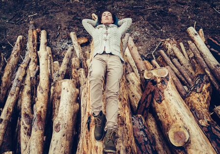 Beautiful young woman with blue hair lying on stack of felled tree trunk. Hiker girl resting outdoorの写真素材