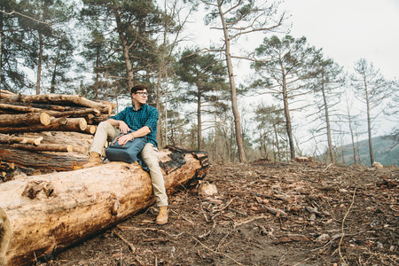 Hiker young man with backpack sitting on felled wood trunks in the forest outdoorの写真素材
