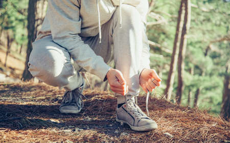 Unrecognizable sportsman runner tying shoelaces outdoor near the tree at sunny dayの写真素材