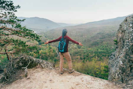 Traveler young woman with backpack standing with raised arms and enjoying view of mountains, rear viewの写真素材