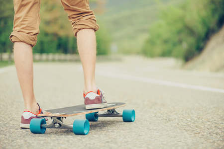 Unrecognizable guy standing on longboard on road in summer, view of legs