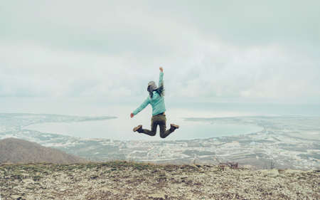 Happy traveler young woman jumping on mountain on background of sea bay, rear viewの写真素材