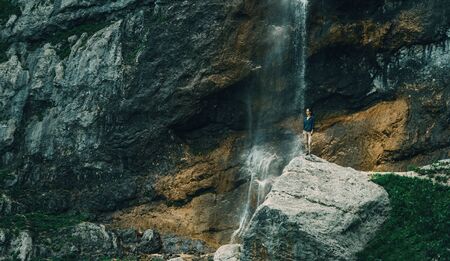 Traveler young woman standing on rocky stone near the waterfall in summerの写真素材