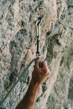 Male climber holding rope and quick-draw on rock wall outdoor. Close-up of handの写真素材
