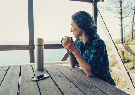 Young woman resting with cup of tea on wooden terrace in summerの写真素材