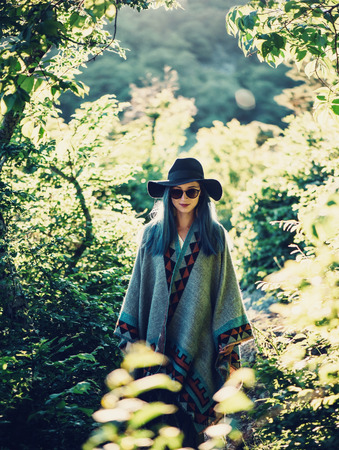Boho style girl in hat and poncho walking in summer park at sunny dayの写真素材