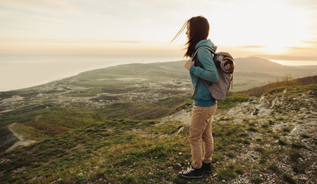 Beautiful traveler young woman with backpack walking in mountains at sunsetの写真素材