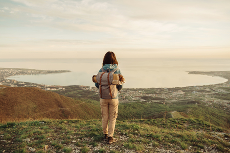 Traveler explorer young woman with backpack standing on peak of mountain and enjoying view of sea bayの写真素材