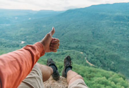 Traveler young man showing thumb up in summer mountains, point of view shotの写真素材