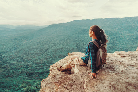 Traveler young woman sitting on edge of cliff and looking on mountains in summer. Toned imageの写真素材