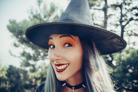 Portrait of cheerful witch. Young woman in costume of Halloween witch looking at camera