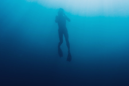 Silhouette of young man free diver swimming underwater in blue deep seaの写真素材