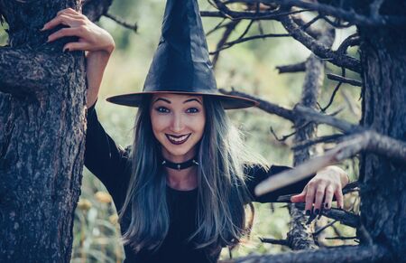 Cheerful young witch walking among old dry trees, looking at cameraの写真素材