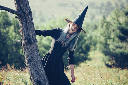 Smiling young woman wearing in costume of witch walking in autumn forest outdoor. Halloween themeの写真素材