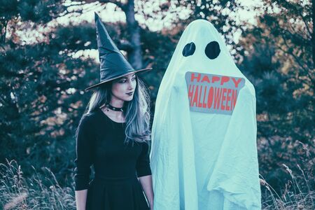 White ghost with poster and witch walking in autumn forest. Halloween themeの写真素材