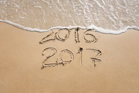 Old year 2016 and new year 2017 written on sand near the sea, wave washes away 2016の写真素材